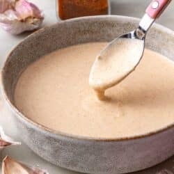 Spoon dipping into smoky garlic aioli in a small bowl.
