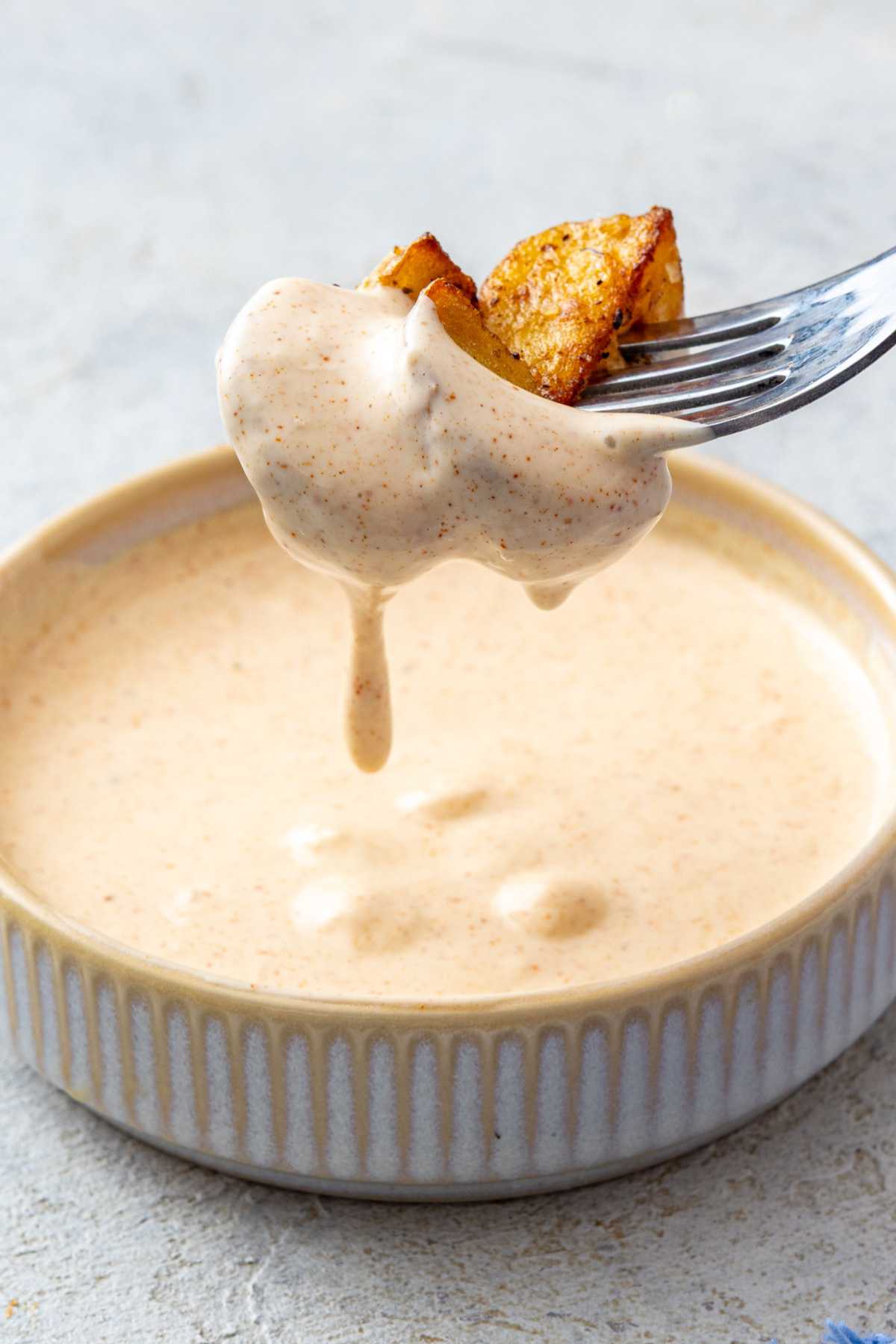 Dipping roasted potatoes into a garlic mayo sauce in a small bowl.