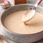 Spoon dipping into smoky garlic aioli in a small bowl.