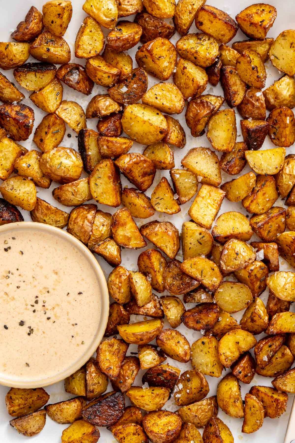 Pan fried potatoes on a plate with a small bowl of dipping sauce.