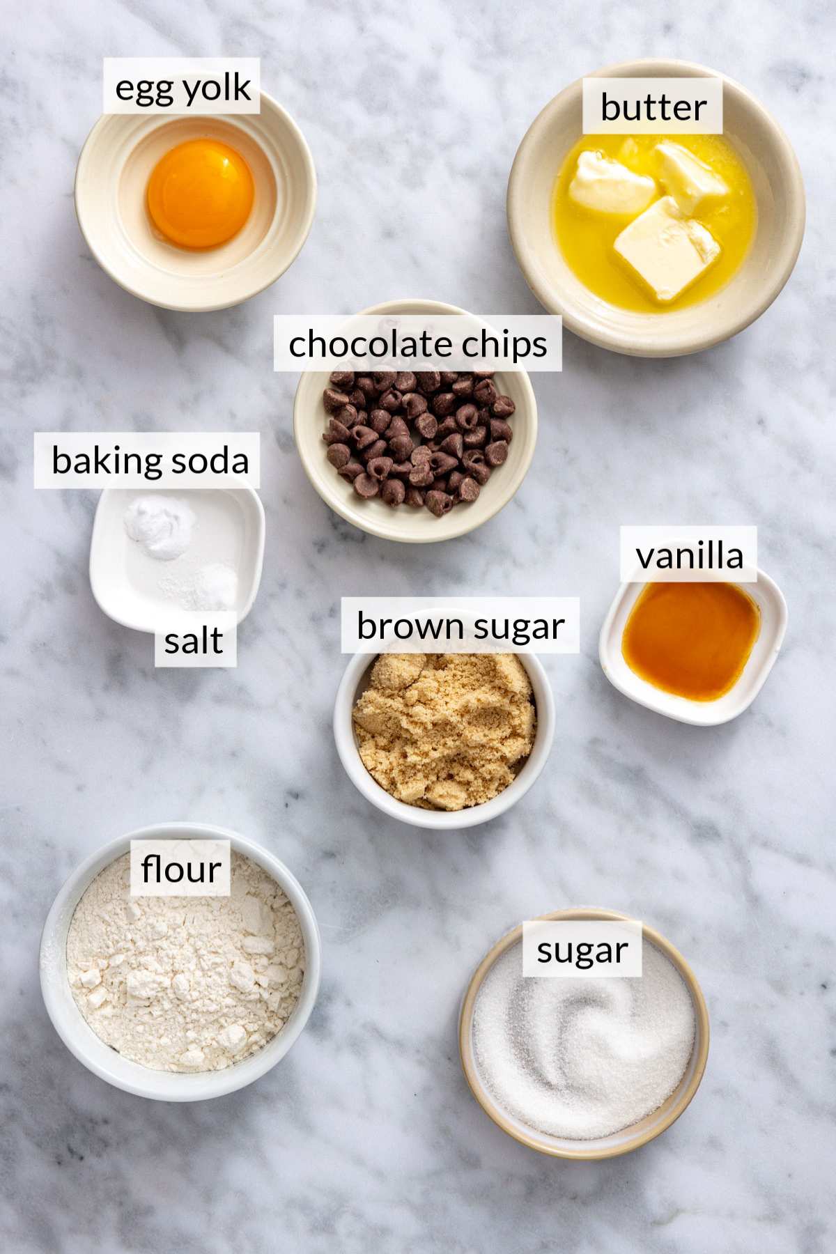 Small bowls with an egg yolk, butter, chocolate chips, sugar and flour.