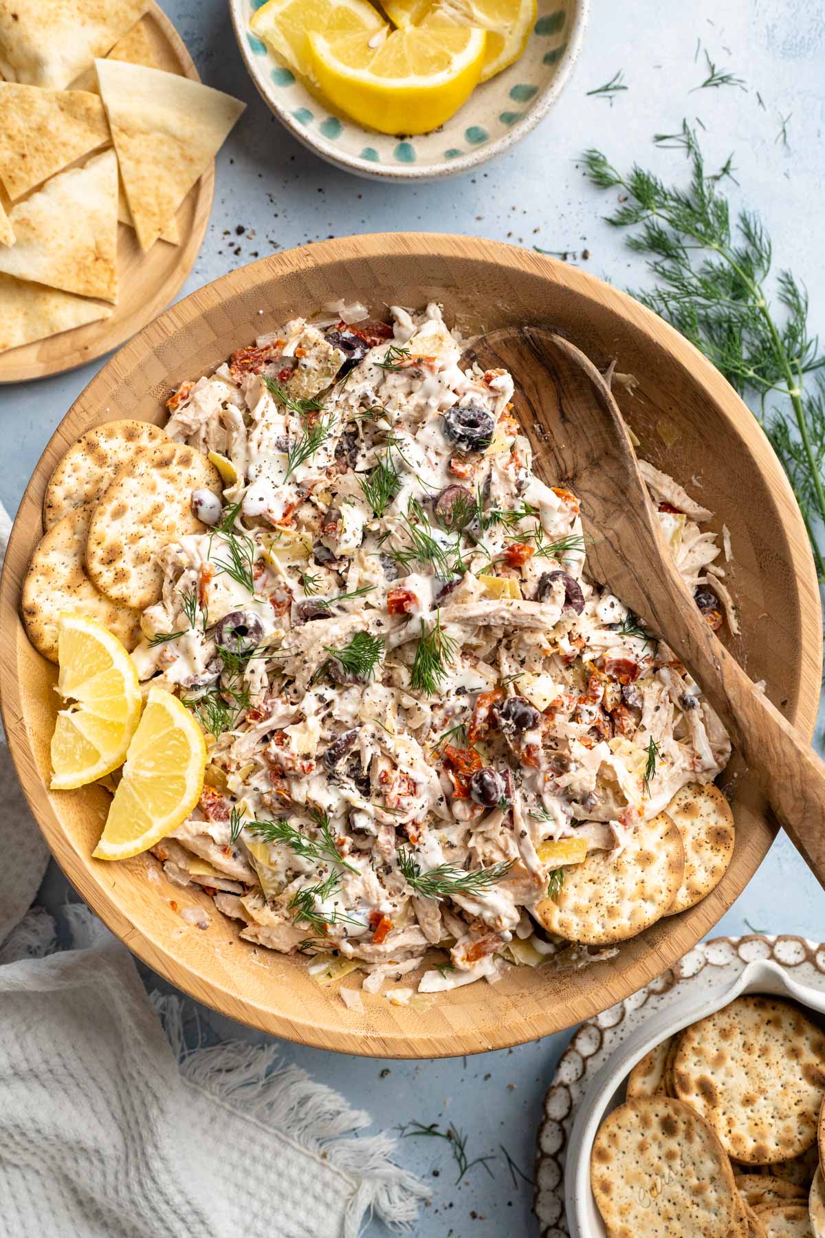 Greek chicken salad garnished with fresh dill and served with lemon wedges.