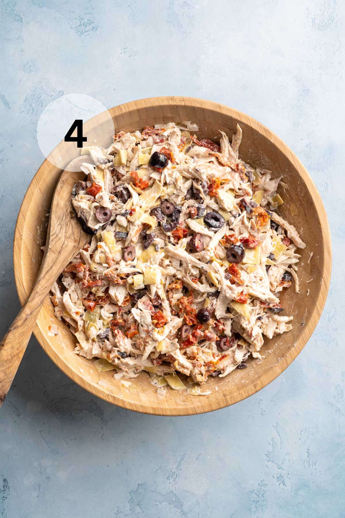 Greek chicken salad in a large bowl with a wooden spoon.