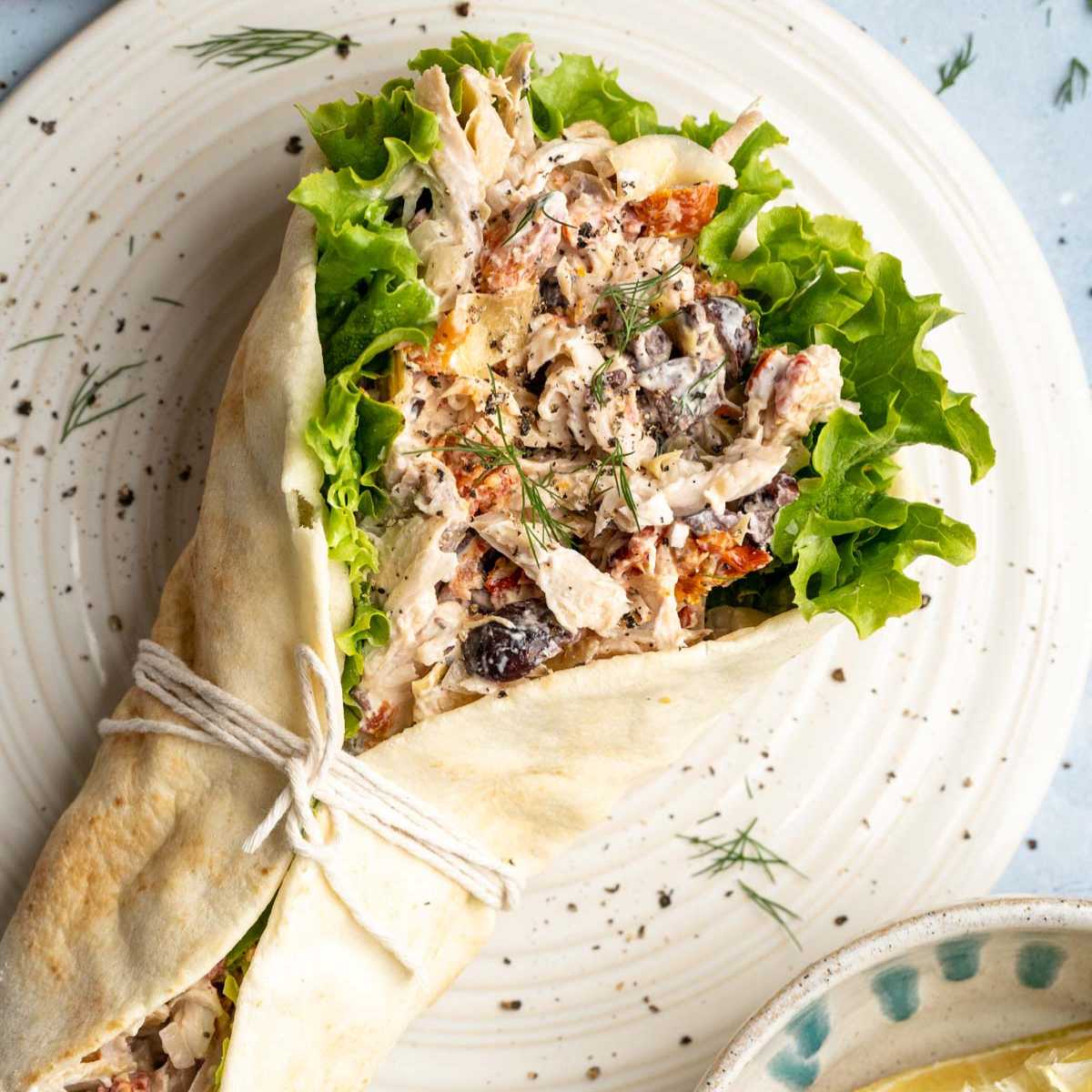 Greek chicken salad in a wrap served on a plate.