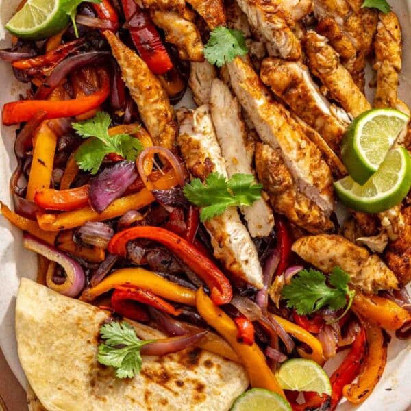 Sliced grilled chicken on a platter with charred veggies and tortillas.