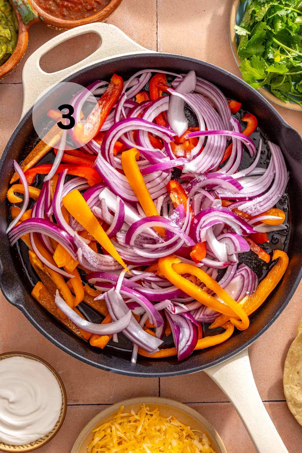 Red onion and bell pepper strips cooking in a skillet.