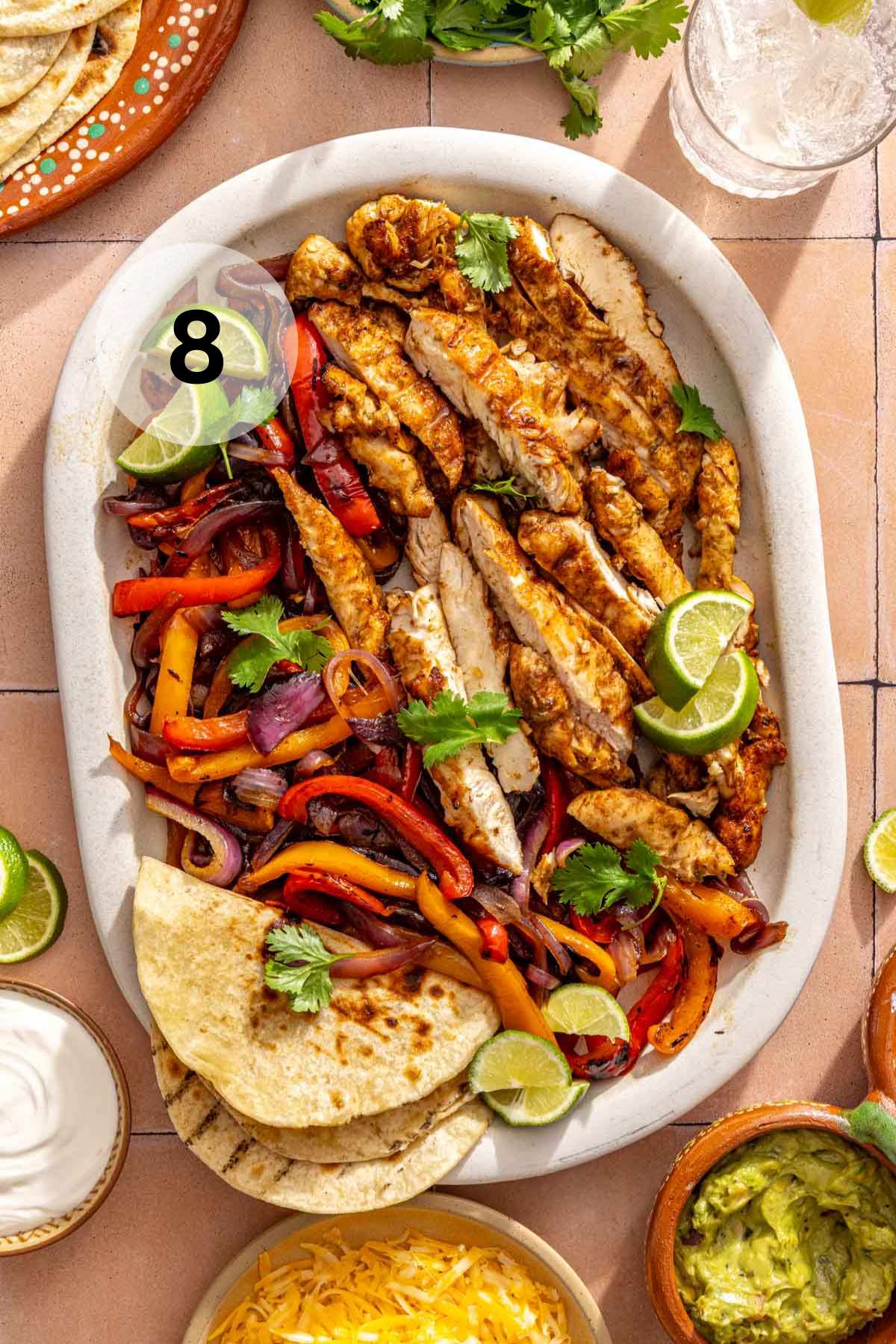 Grilled fajita chicken on a platter with caramelized veggies and tortillas.