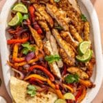 Sliced grilled chicken on a platter with charred veggies and tortillas.