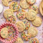 Sprinkle cookies on parchment paper with one cookie in a small bowl of sprinkles.