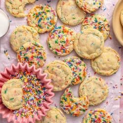 Sprinkle cookies on parchment paper with one cookie in a small bowl of sprinkles.