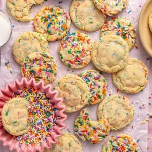 Sprinkle cookies on parchment paper with one cookie in a small bowl of sprinkles.