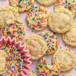 Sprinkle cookies on parchment paper with one cookie in a small bowl of sprinkles.