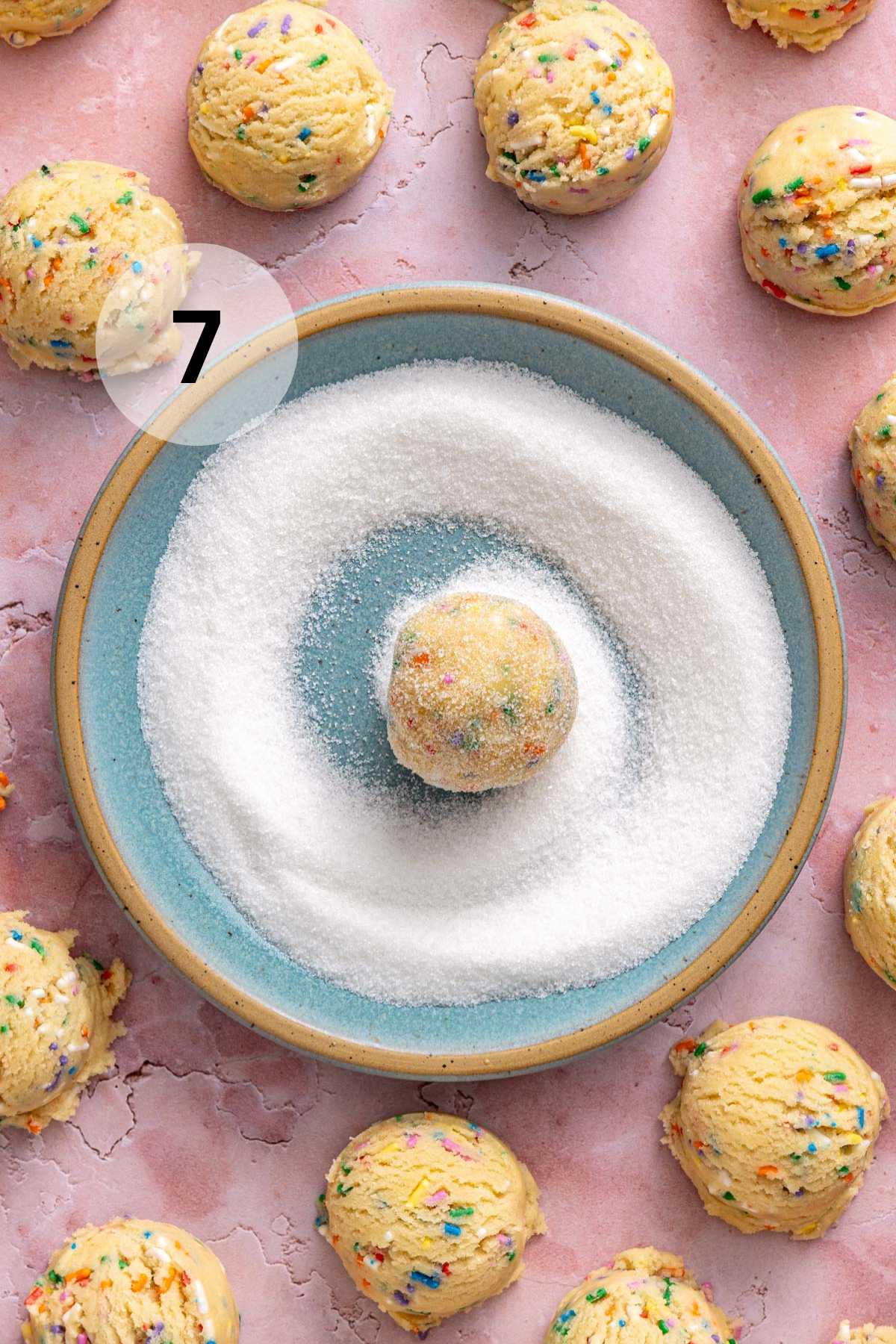 Rolling a cookie dough ball in granulated sugar.