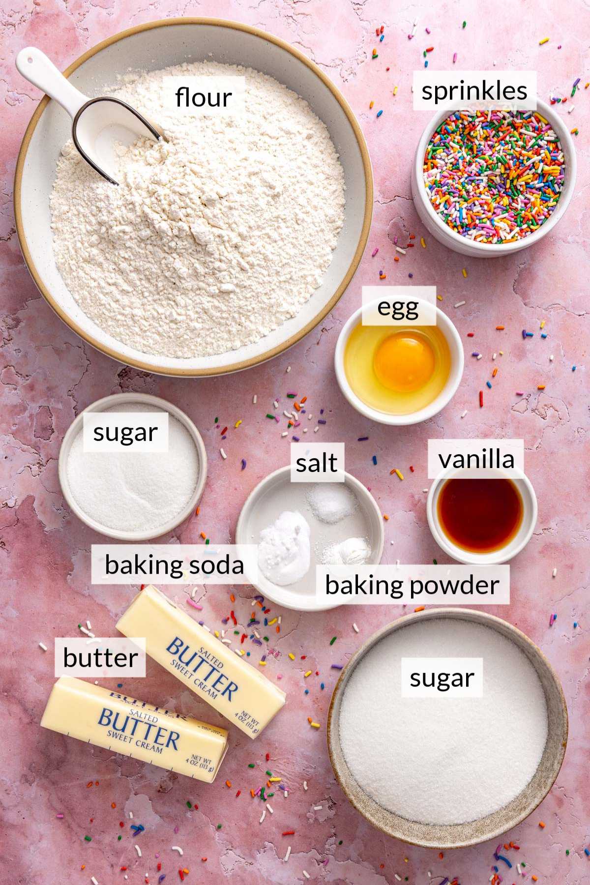 Small bowls with flour, egg, sprinkles, sugar and vanilla near sticks of butter.