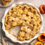 Peach pie in a white pie plate with one piece missing.