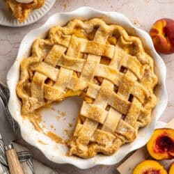 Peach pie in a white pie plate with one piece missing.