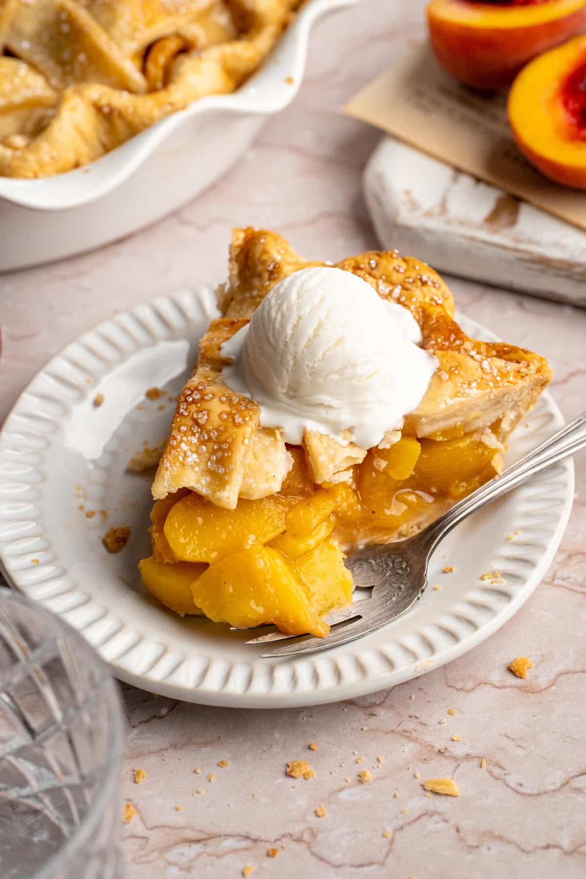Slice of peach pie topped with a scoop of vanilla ice cream.