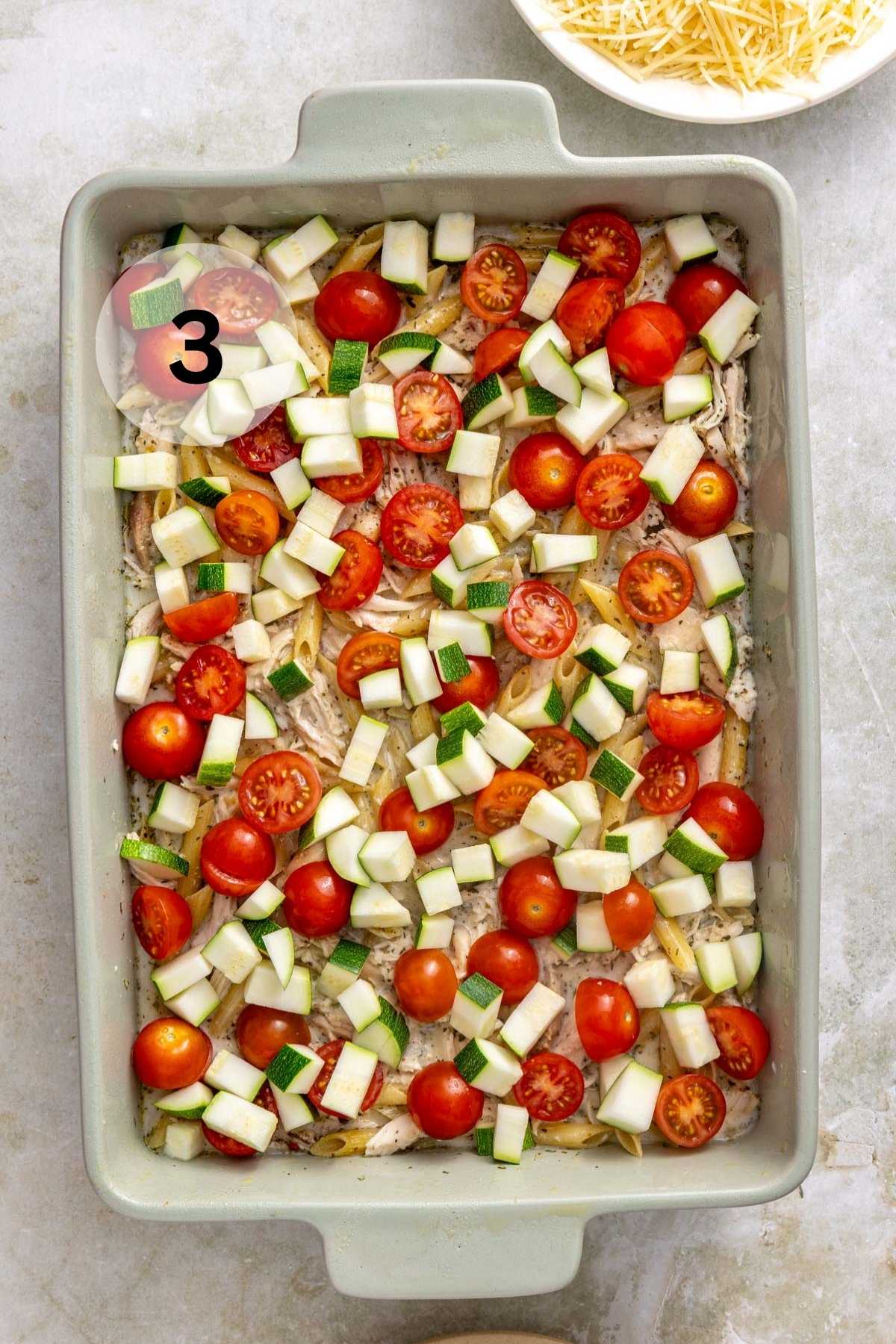 Tomatoes and chopped zucchini layered over pasta and chicken in a casserole dish.