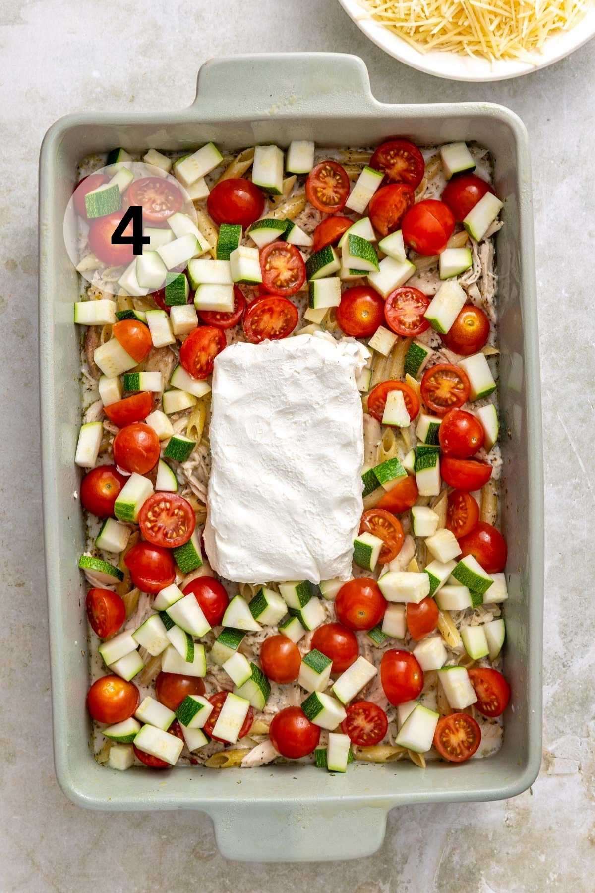 Block of cream cheese in the center of a baking dish with tomatoes and zucchini.