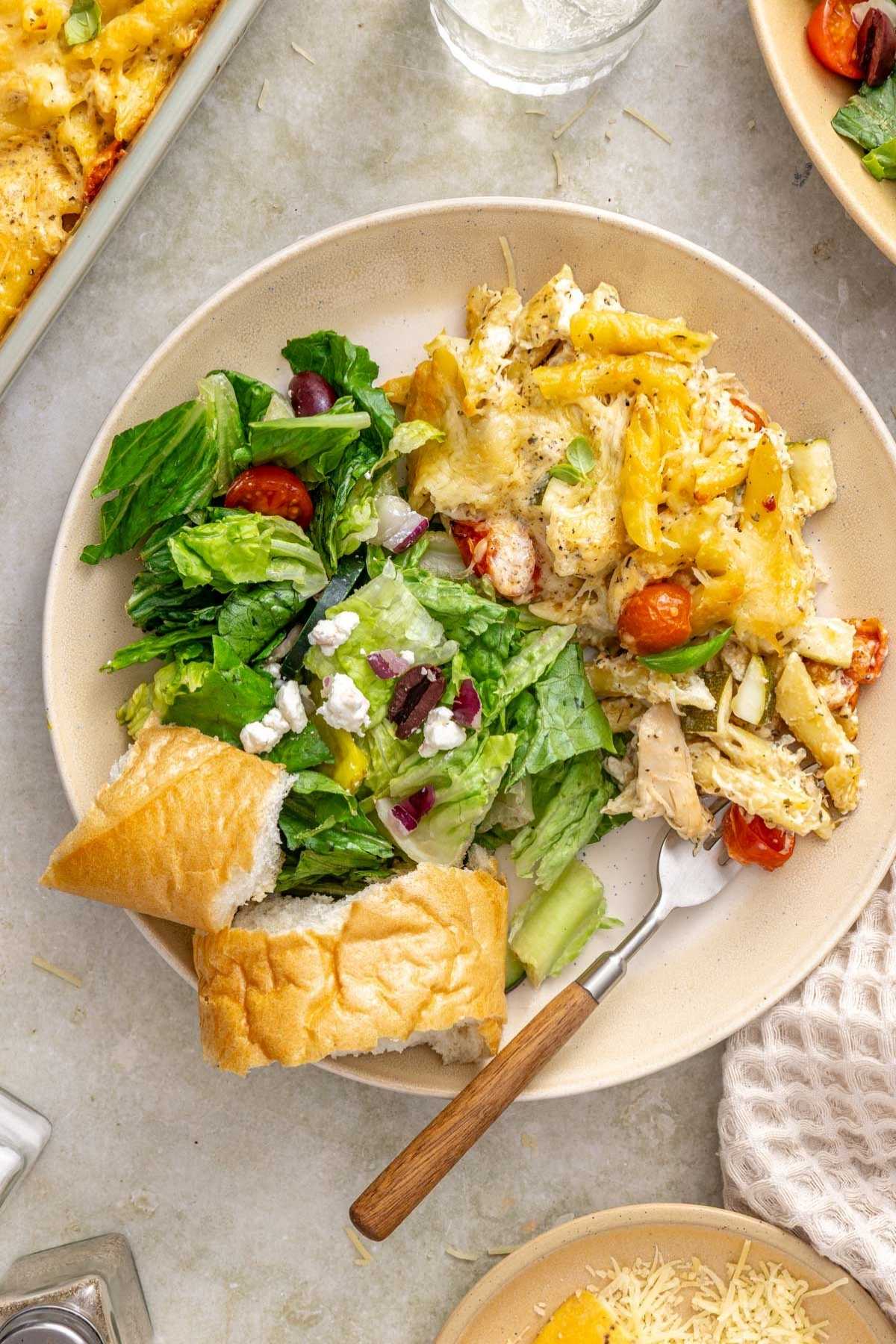 Chicken pasta bake served on a plate with a salad and bread.