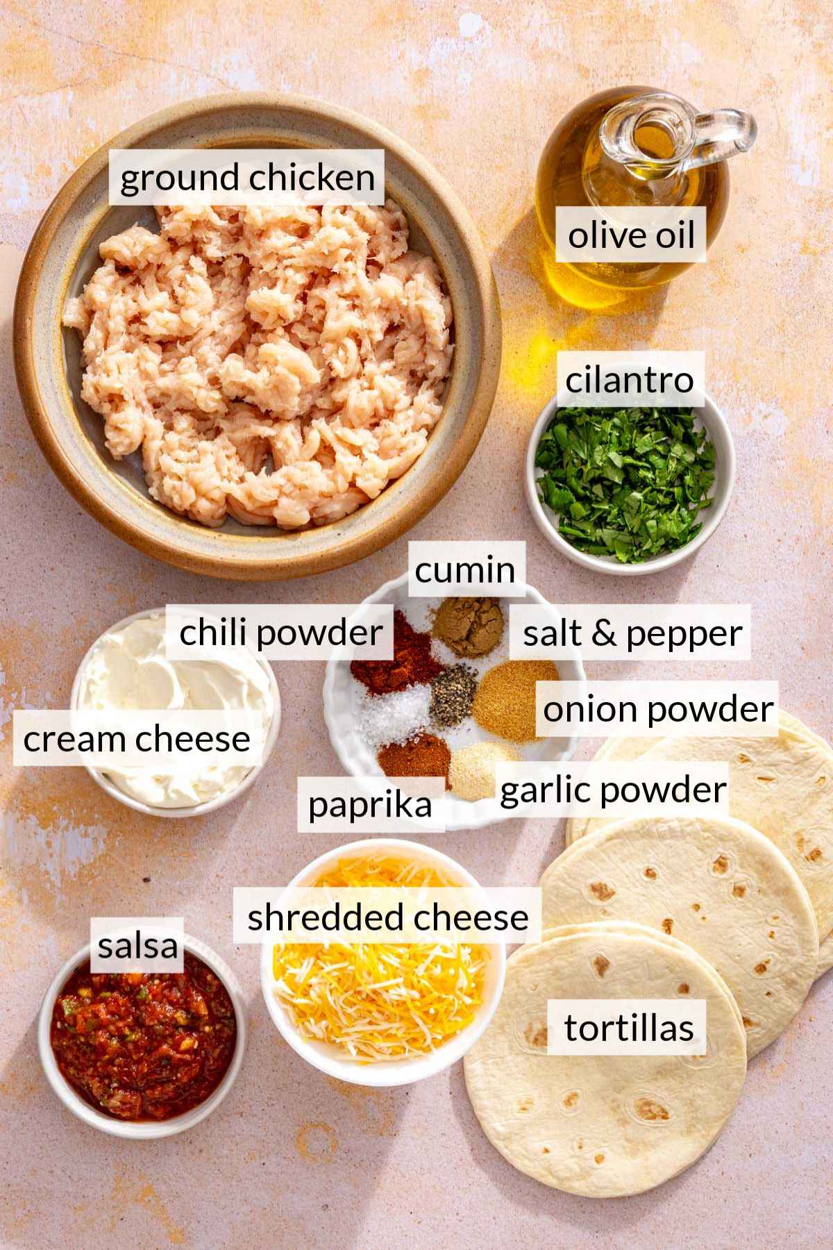A bowl of uncooked ground chicken near small bowls of cheese, salsa and cream cheese.