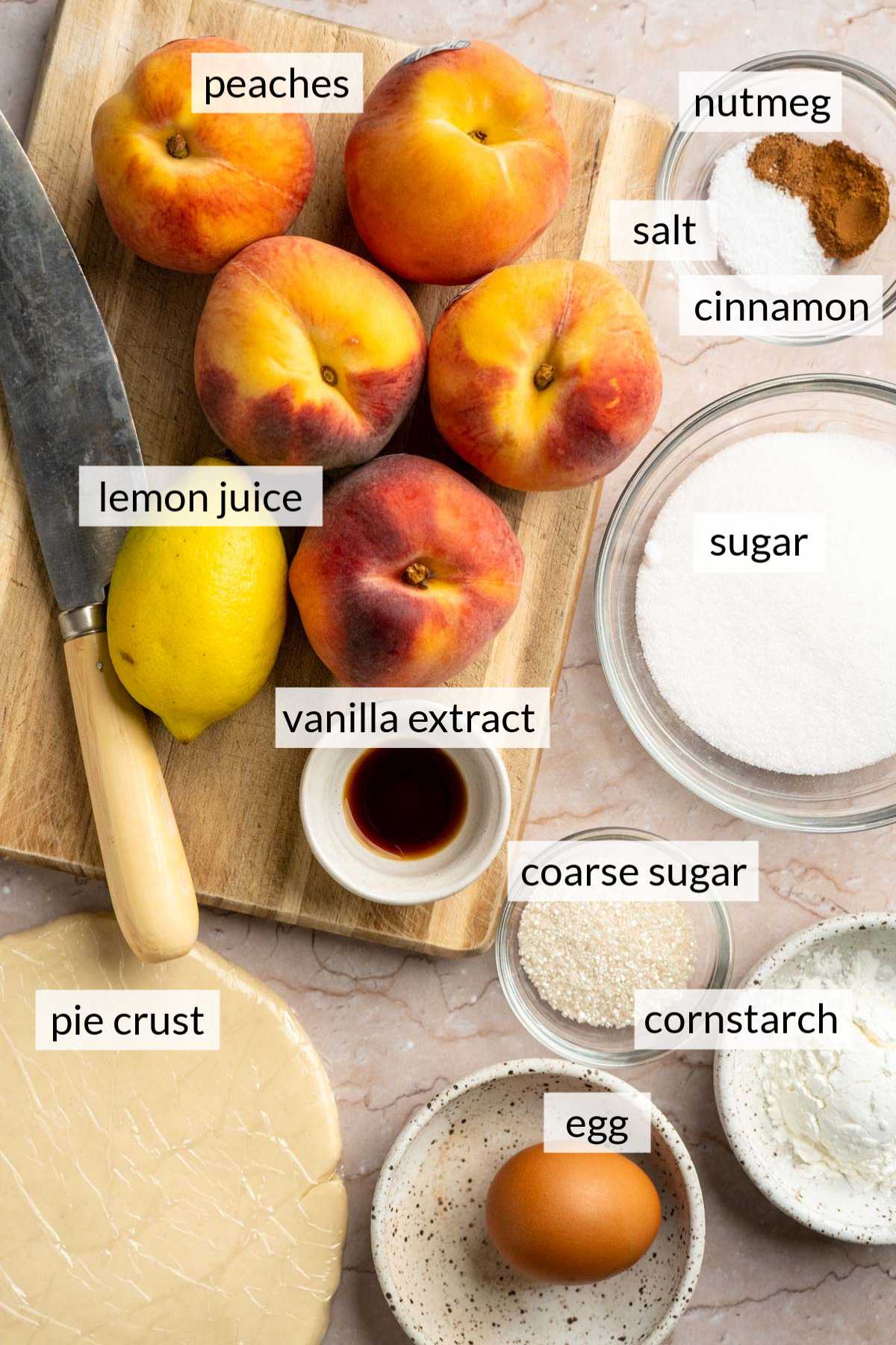 Peaches on a cutting board near pie crust and small bowls of sugar, vanilla, cinnamon and an egg.