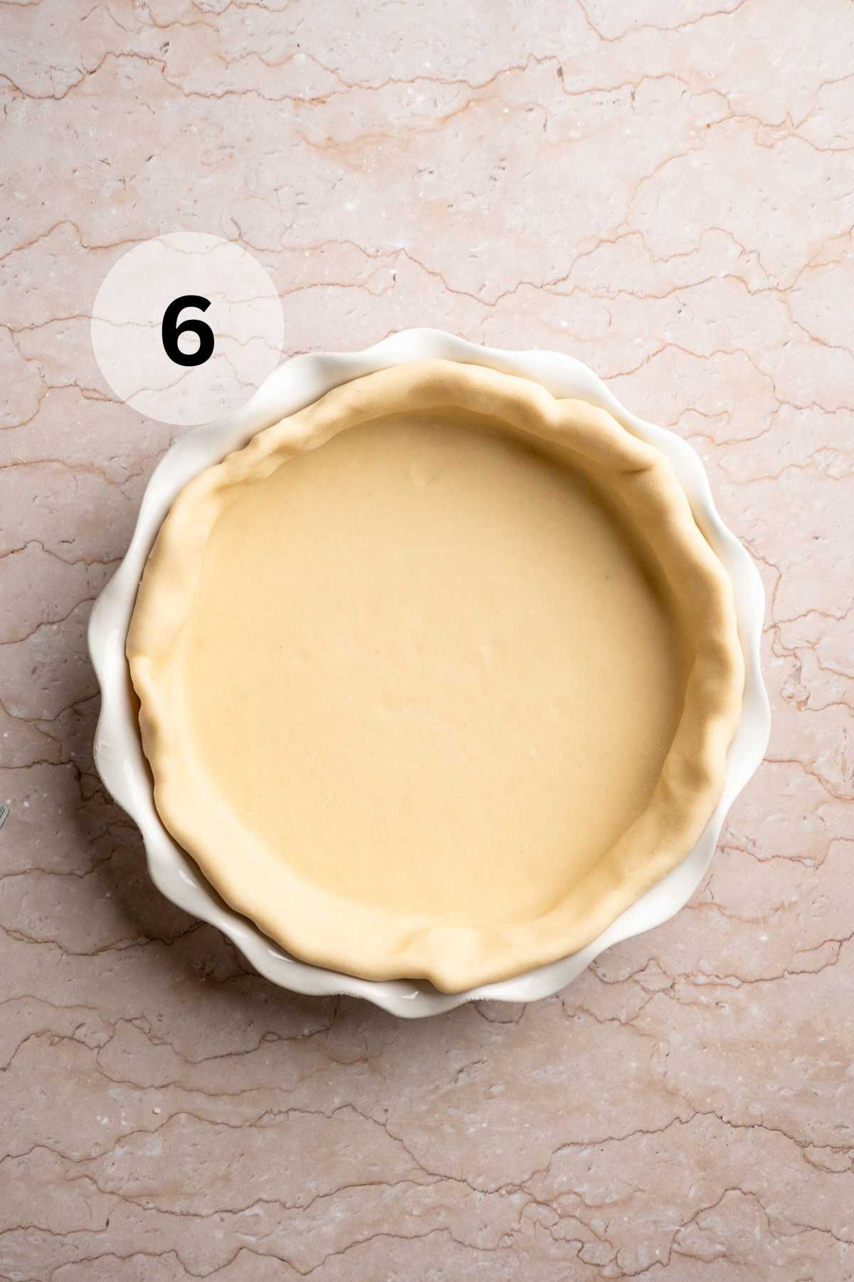 Pie crust in the bottom of a pie plate with sides folded over.
