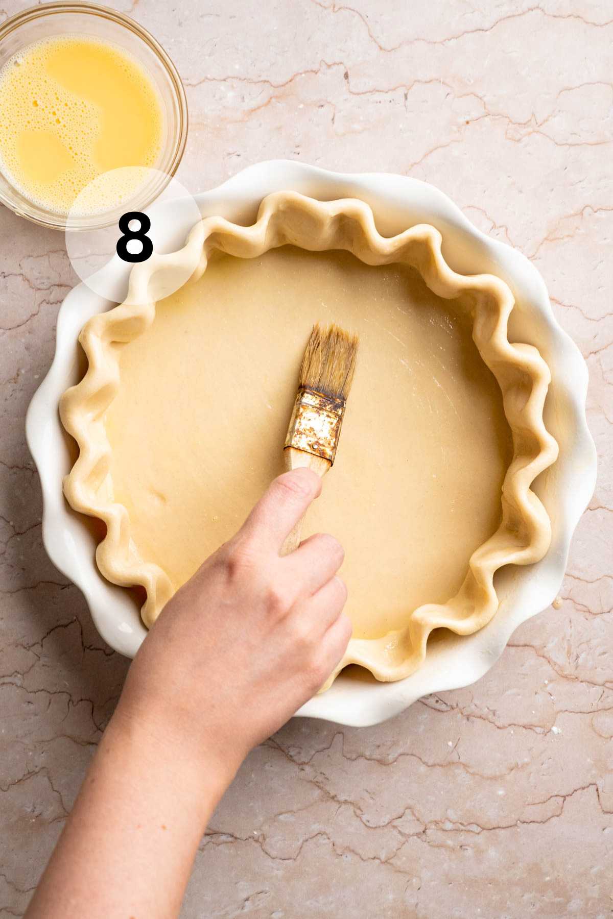 Brushing the bottom of a pie crust with an egg wash.