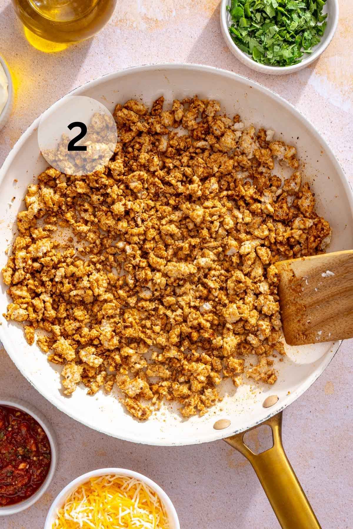 Using a wooden spoon to stir seasoned chicken in a white skillet.