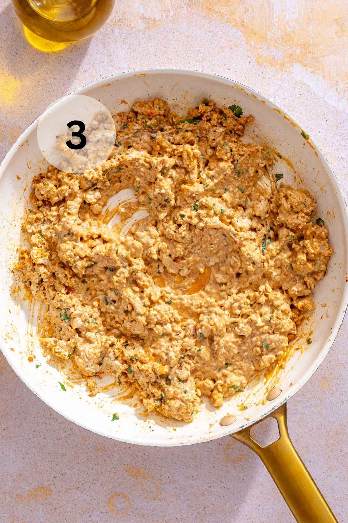 The cream cheese and seasoned chicken mixture in a white skillet.