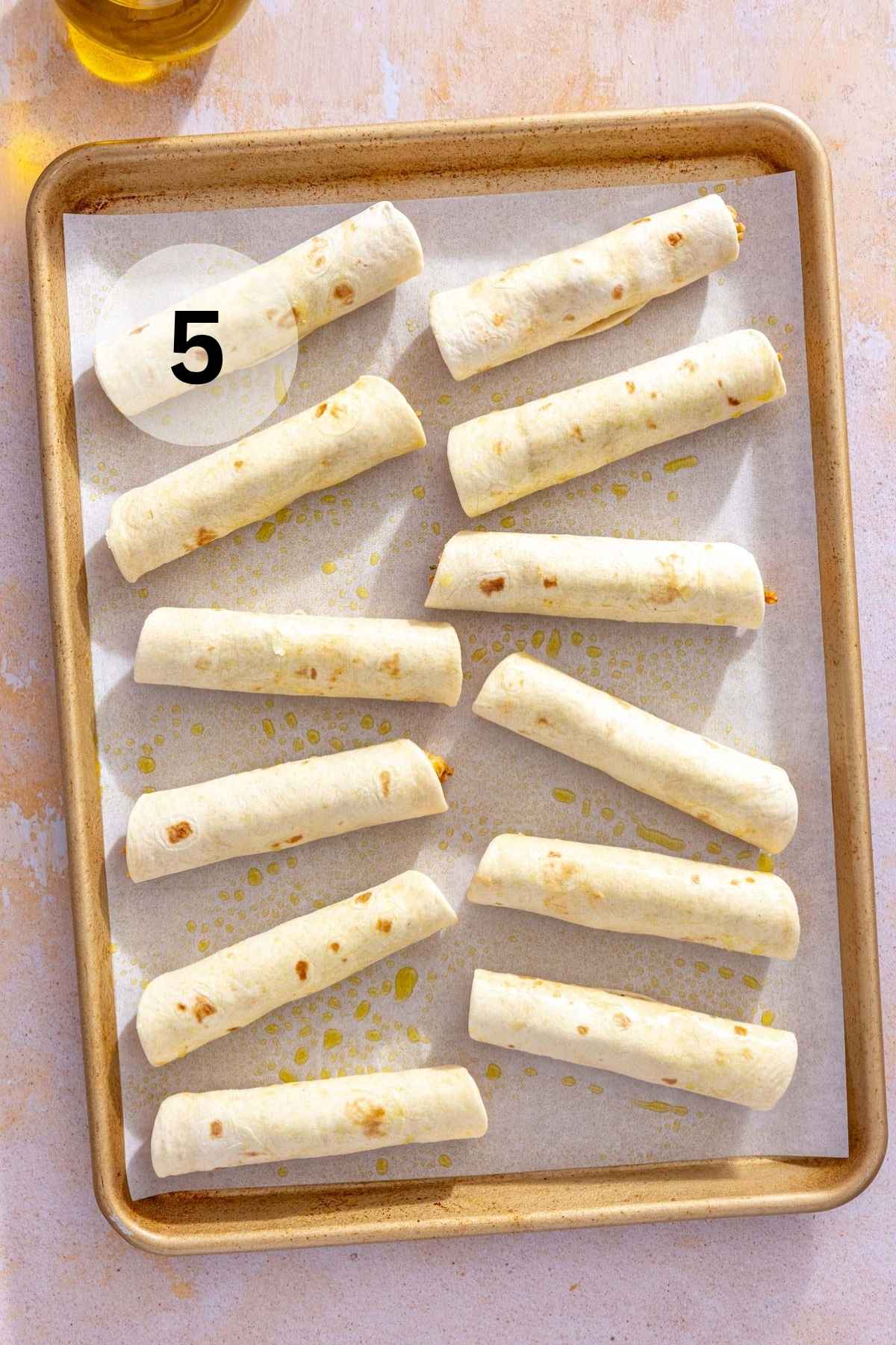 Rolled taquitos on a lined baking sheet.