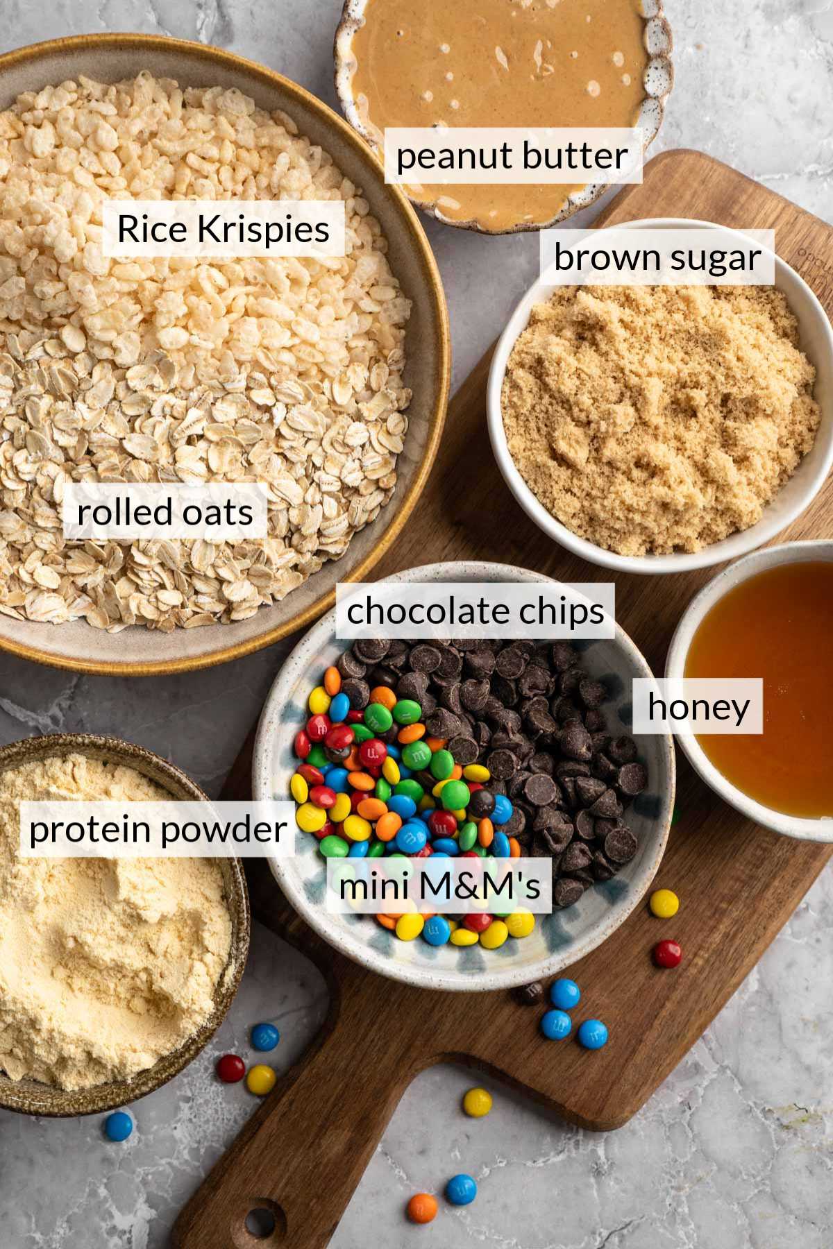 Small bowls with ingredients like oats, rice krispies, chocolate chips, brown sugar, and honey.