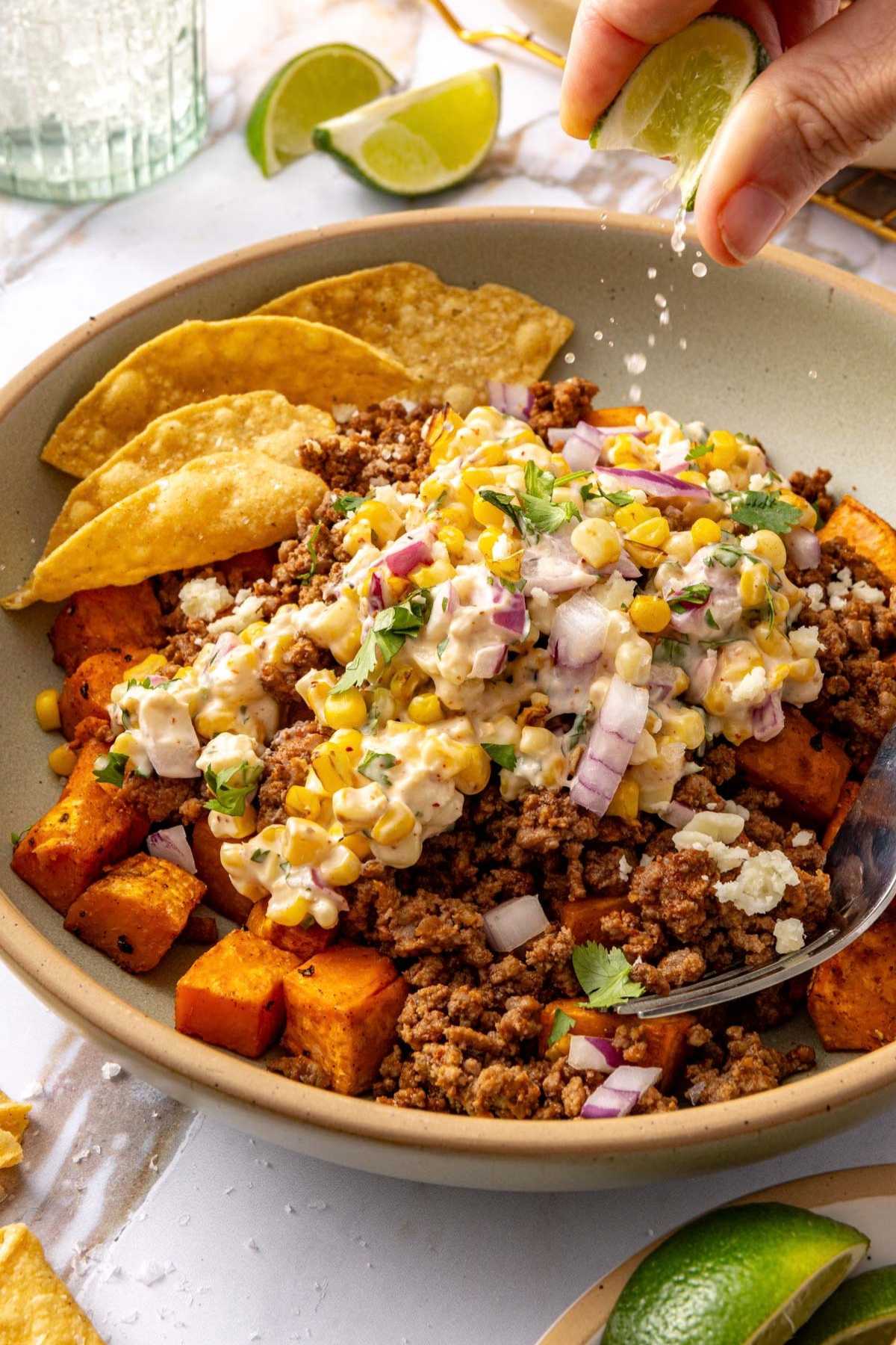 Squeezing lime over a sweet potato ground beef bowl with street corn.