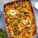 Taco potatoes in a casserole dish topped with guacamole and sour cream.