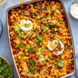 Taco potatoes in a casserole dish topped with guacamole and sour cream.