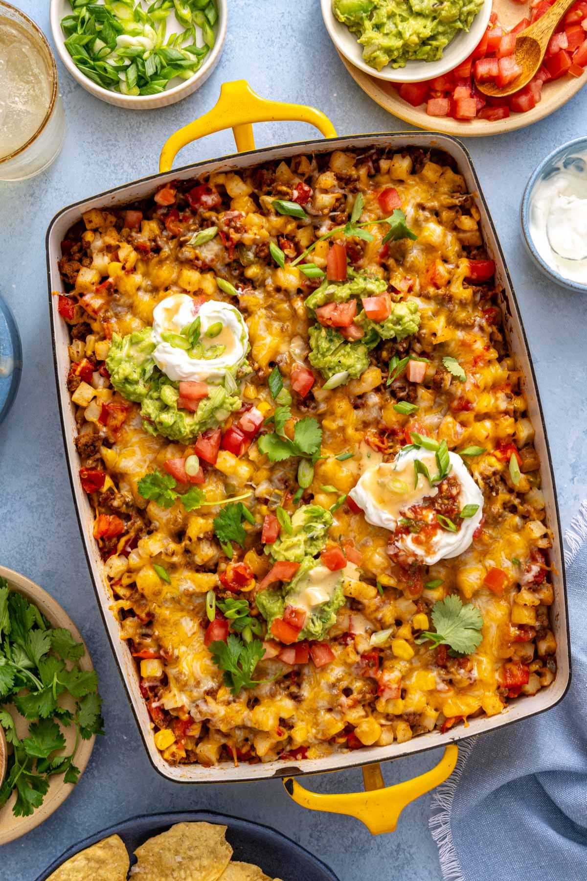 Taco potatoes in a casserole dish topped with guacamole and sour cream.