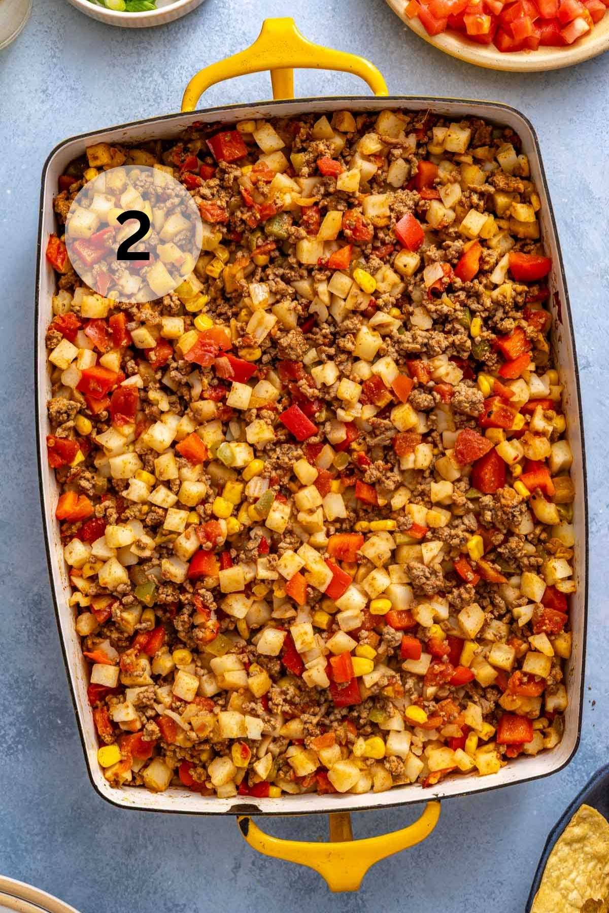 Mixture of diced potatoes, red bell pepper and beef in a casserole dish.